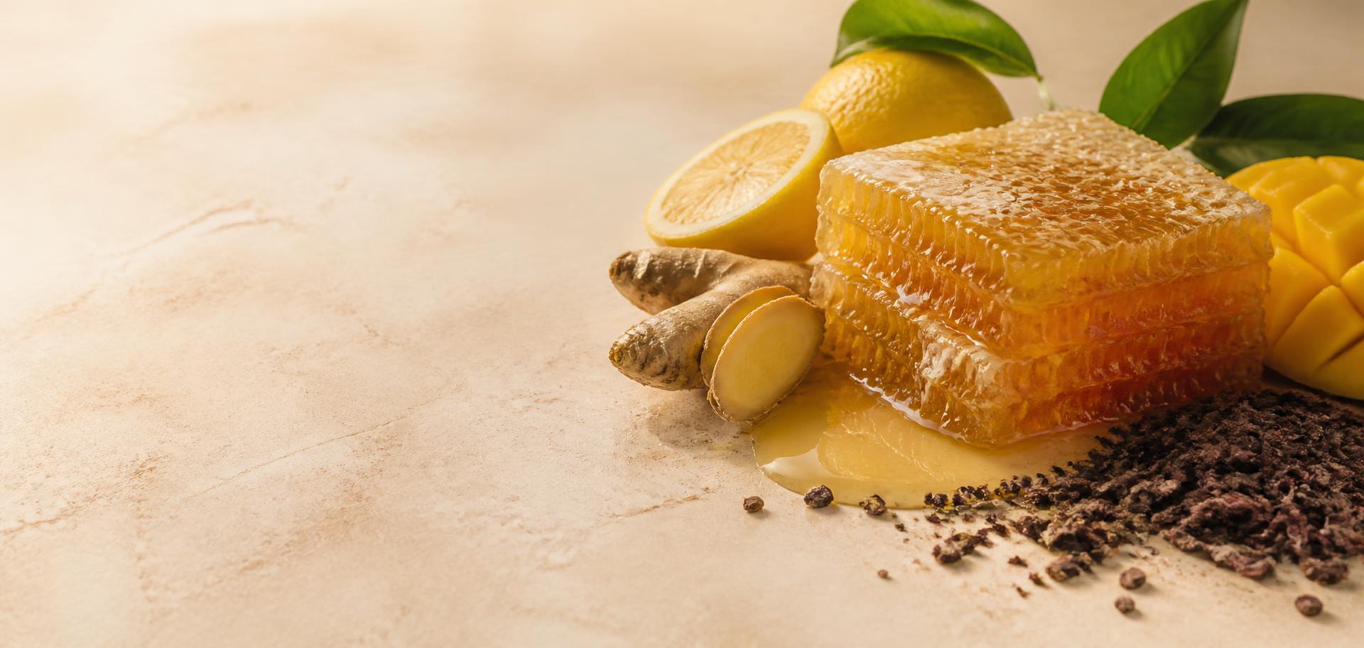 Honeycomb dripping with raw honey beside lemon, ginger, mango and cocoa